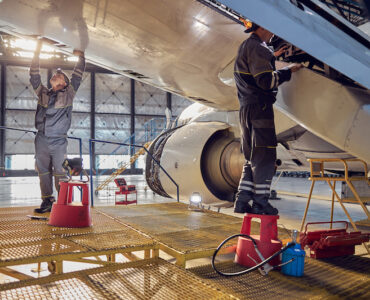 Full length side view portrait of men aviation mechanics fixing and checking spoiler and flaps on the airplane