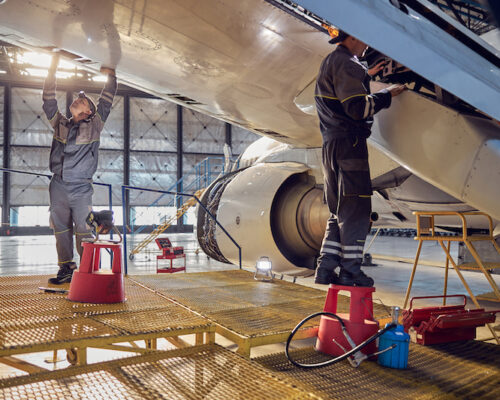 Full length side view portrait of men aviation mechanics fixing and checking spoiler and flaps on the airplane